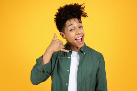 Photo for Cool black guy making a call me hand gesture with a joyful expression on a yellow backdrop - Royalty Free Image