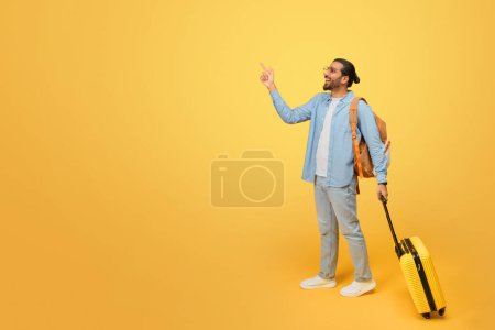 Téléchargez les photos : Homme indien en déplacement, saluant un taxi avec bagages à la main prêt pour une aventure montrée sur un fond jaune accrocheur - en image libre de droit