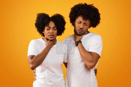 Unhealthy sick african american couple suffering from pain in throat, ill millennial black man and woman touching their throats, have cold or flu, tonsilitis, isolated on yellow background