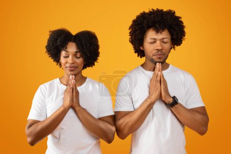 Téléchargez les photos : Homme et femme afro-américains concentrés millénaires, les yeux fermés, priant ensemble sur fond de studio jaune, les mains sur la poitrine. Religion, concept de croyances - en image libre de droit