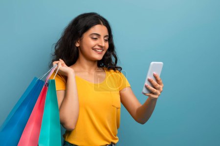 Glückselige junge Frau genießt ihr Handy mit Einkaufstüten in der Hand und betont digitales Engagement