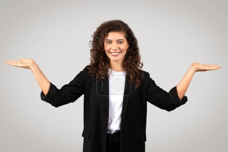 A professional woman in business attire with a pleasant smile makes a balancing gesture with palms facing up