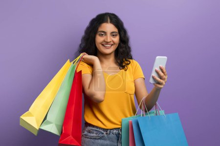 Une femme dans un haut jaune sourit tenant des sacs à provisions et un smartphone, suggérant une expérience d'achat positive