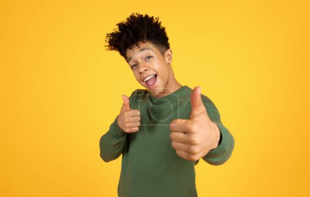 Smiling black man in casual wear giving thumbs up with both hands on a vibrant yellow background