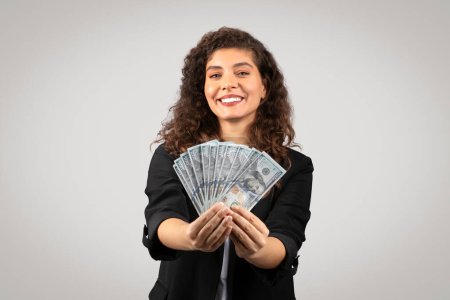 Foto de Mujer de negocios alegre muestra una propagación de la moneda estadounidense, lo que sugiere el éxito o el ahorro - Imagen libre de derechos