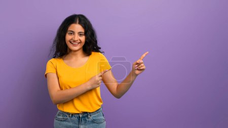 A happy woman with a big smile pointing fingers in two different directions, purple background