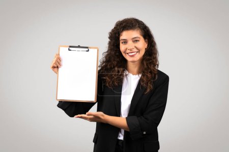 Téléchargez les photos : Jeune femme professionnelle souriant et tenant un presse-papiers avec un papier vierge, parfait pour les maquettes - en image libre de droit