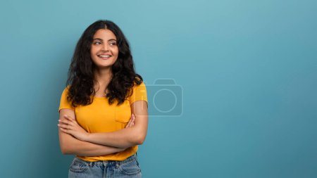 Photo for Contemplative woman with curly hair crossing her arms, looking away, against a blue background - Royalty Free Image