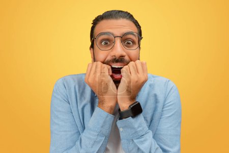 Photo for An anxious looking indian man with hands on his face against a plain yellow background, portraying stress - Royalty Free Image