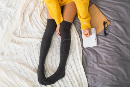 Photo for Girl sitting on bed and making notes to her diary, top view - Royalty Free Image