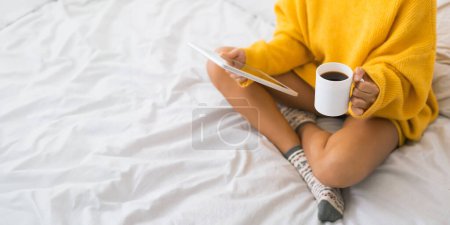 Téléchargez les photos : Femme avec tasse de café et tablette numérique, assise sur le lit, culture - en image libre de droit