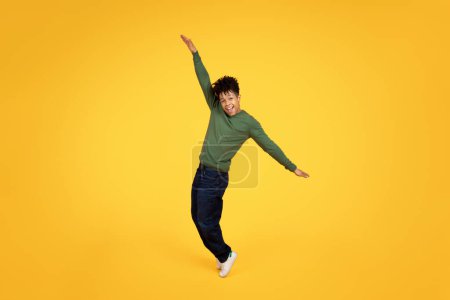 Exuberant young african american man mid-jump with arms outstretched and a joyous expression on yellow background
