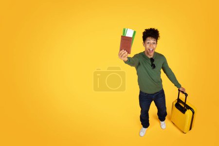 Foto de Un joven afroamericano viajero mostrando un pasaporte y una tarjeta de embarque con una expresión alegre sobre un fondo amarillo sólido - Imagen libre de derechos