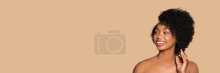 Téléchargez les photos : Radieuse jeune femme noire aux cheveux naturels bouclés regardant loin de l'espace libre avec un sourire joyeux, posant sur fond beige, incarnant la beauté naturelle, bannière publicitaire - en image libre de droit