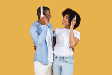 Téléchargez les photos : Heureux couple afro-américain millénaire portant des écouteurs blancs assortis, s'engageant dans une expérience musicale partagée avec des sourires brillants, créant un moment personnel ensemble - en image libre de droit
