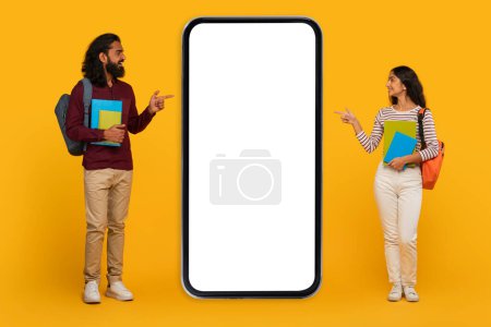 Photo for Young, trendy-dressed man and woman pointing to a blank smartphone screen mockup on a yellow background - Royalty Free Image