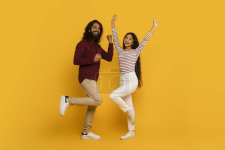 Téléchargez les photos : Homme et femme énergiques sautent avec les bras levés et des expressions élogieuses sur fond jaune - en image libre de droit
