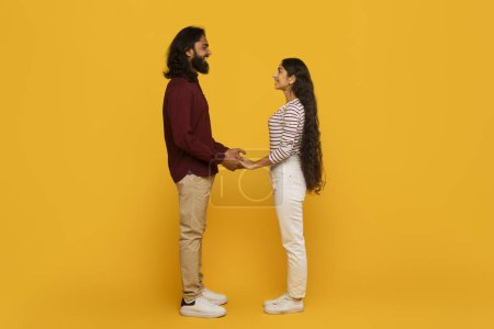Téléchargez les photos : Un homme et une femme se tiennent la main, face à face sur un fond jaune vif, dépeignant un sentiment de connexion et de convivialité - en image libre de droit