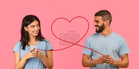 Photo for A young woman with gentle smile, hold smartphone, glances at bearded man also with phone, both connected by red heart line on pink background, symbolizing a happy digital connection - Royalty Free Image