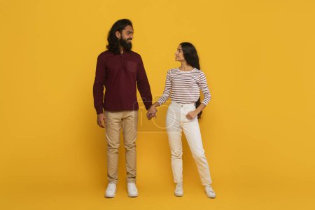Téléchargez les photos : Un homme et une femme vêtus avec désinvolture, partageant un moment de rire sur un fond jaune vif - en image libre de droit