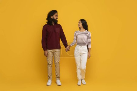 Foto de Un hombre y una mujer con atuendo casual se miran afectuosamente el uno al otro con un fondo amarillo - Imagen libre de derechos