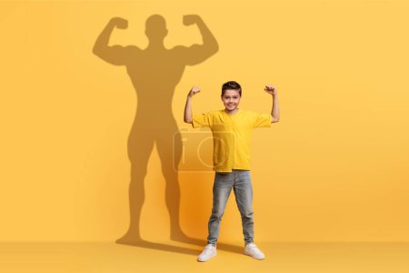 Foto de Un joven entusiasta con una camisa amarilla flexiona sus brazos con confianza, su silueta sobre un fondo amarillo a juego que proyecta la fuerte figura de un superhéroe, encarnando la aspiración - Imagen libre de derechos