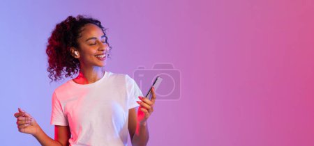 Fröhliche junge Frau tanzt, während sie ihr Smartphone vor den Hintergrund eines Gefälles hält