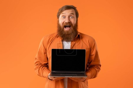 Photo for Great Website. Excited Redhaired Bearded Man Holding Laptop Computer With Empty Screen And Exclaiming In Excitement, Showing Mockup Place For Online Offer, On Orange Background - Royalty Free Image