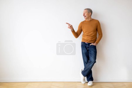 Photo for A casually dressed man stands against a blank wall, pointing to something off-camera with a look of interest or emphasis - Royalty Free Image