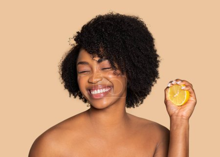 Strahlende schwarze Frau mit Zitronenscheibe, ihr Lächeln mit geschlossenen Augen, das natürliche Hautpflege-Begeisterung und Frische auf sanftem beigem Hintergrund ausstrahlt