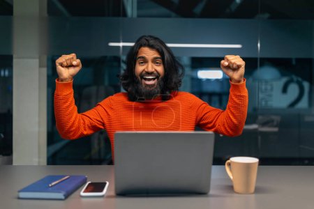 Foto de El hombre entusiasta con los puños levantados en la alegría delante de su portátil en un escritorio - Imagen libre de derechos