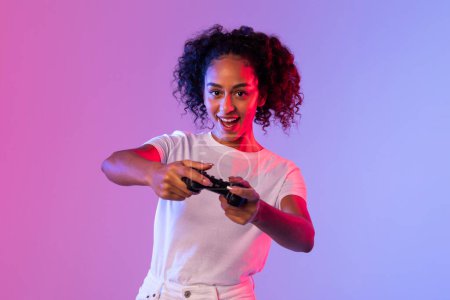 Mujer joven que se divierte jugando con un controlador de juego negro en frente de un fondo de doble tono