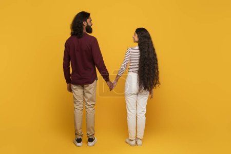 Eine Rückansicht eines Mannes und einer Frau, die Hand in Hand gehen, der gelbe Hintergrund weckt Wärme und Optimismus für zukünftige Wege.