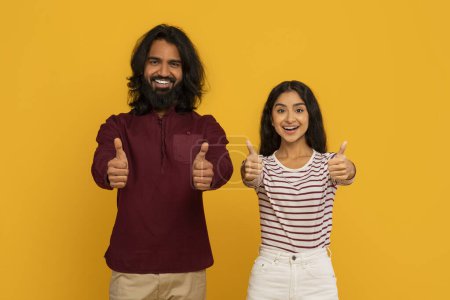 Téléchargez les photos : Les deux confiants donnant un pouce levé, un homme et une femme se tiennent côte à côte, exsudant l'approbation et la positivité sur le jaune - en image libre de droit