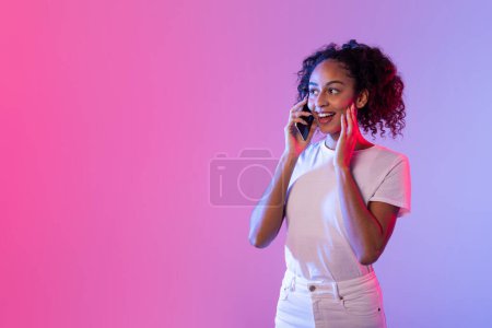A young woman happily chatting on a smartphone with a vibrant pink and purple neon background