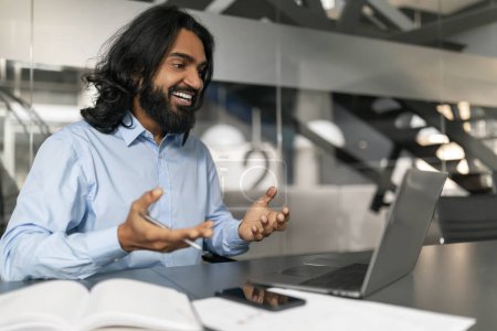Foto de Hombre profesional en una camisa azul que trabaja desde un espacio de oficina moderno con un ordenador portátil, expresando alegría y satisfacción - Imagen libre de derechos