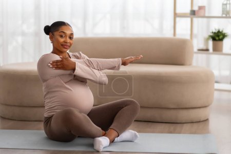 Téléchargez les photos : Mode de vie sain pendant la grossesse. Attente positive jeune femme noire étirant le corps à la maison, assis sur un tapis de yoga, profiter de son entraînement, copier l'espace. Sport pour les futures mamans - en image libre de droit