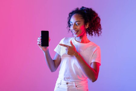 Photo for Smiling woman holding a smartphone towards the camera with a blank screen for mock-ups on a dual-tone backdrop - Royalty Free Image