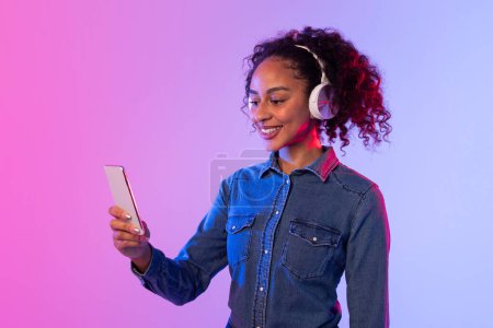 Eine junge Stylistin ist mit Smartphone und Kopfhörer vor zweifarbigem Hintergrund beschäftigt