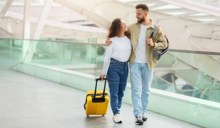 Téléchargez les photos : Voyage ensemble. Couple européen heureux marchant avec des bagages au terminal de l'aéroport, Romantique jeune homme et femme embrassant et souriant à l'autre tout en allant à la porte d'embarquement, Copier l'espace - en image libre de droit