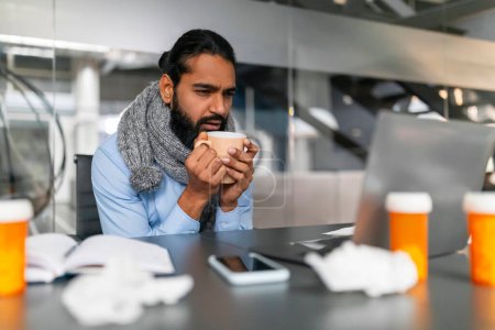 Téléchargez les photos : Homme d'affaires avec une écharpe tenant une tasse, regardant mal car il traite avec se sentir malade pendant qu'il travaille dans le bureau - en image libre de droit