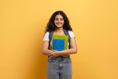 Confident student holding blue notebooks against a yellow background, symbolizing learning and education