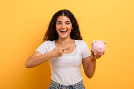 Photo for The womans point towards a piggy bank indicates enthusiasm about savings or financial goals - Royalty Free Image