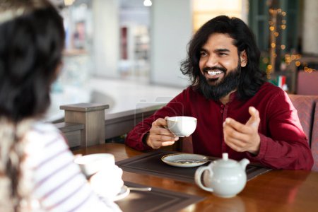 Photo for Handsome indian man with his girlfriend enjoying aromatic coffee and having friendly conversation at city cafe. Romantic eastern couple on first date at canteen, getting to know each other - Royalty Free Image