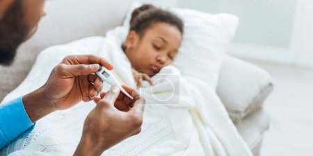 Téléchargez les photos : Enfant malade. Père attentionné mesurant la température de sa fille à la maison - en image libre de droit