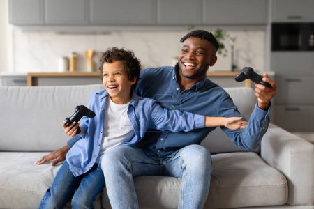 Ein begeistertes Vater-Sohn-Duo lacht fröhlich beim gemeinsamen Videospielen auf der Couch