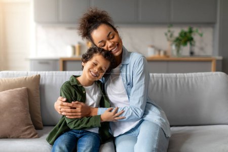 Téléchargez les photos : Une mère et son fils partagent une étreinte chaleureuse sur le canapé, mettant en valeur un moment de famille aimante dans un cadre familial - en image libre de droit