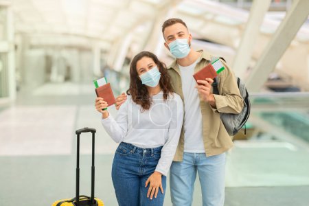 Photo for Happy Young Couple In Medical Face Masks Posing In Airport With Passports And Tickets In Hands, Cheerful European Man And Woman Looking At Camera, Travelling Together During Air Pollution Or Epidemic - Royalty Free Image