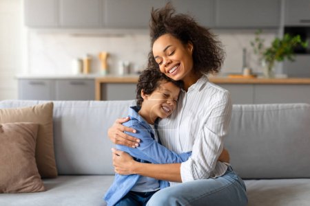 Foto de Mujer sonriente y su hijo se abrazan en una sala de estar iluminada - Imagen libre de derechos