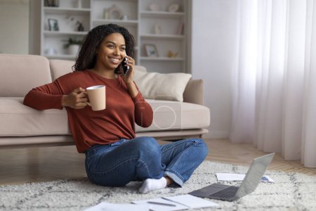 Photo for Remote Job. Smiling Black Woman Talking On Cellphone And Drinking Coffee While Working With Laptop At Home, Happy African American Freelancer Lady Having Phone Call, Enjoying Distance Work - Royalty Free Image